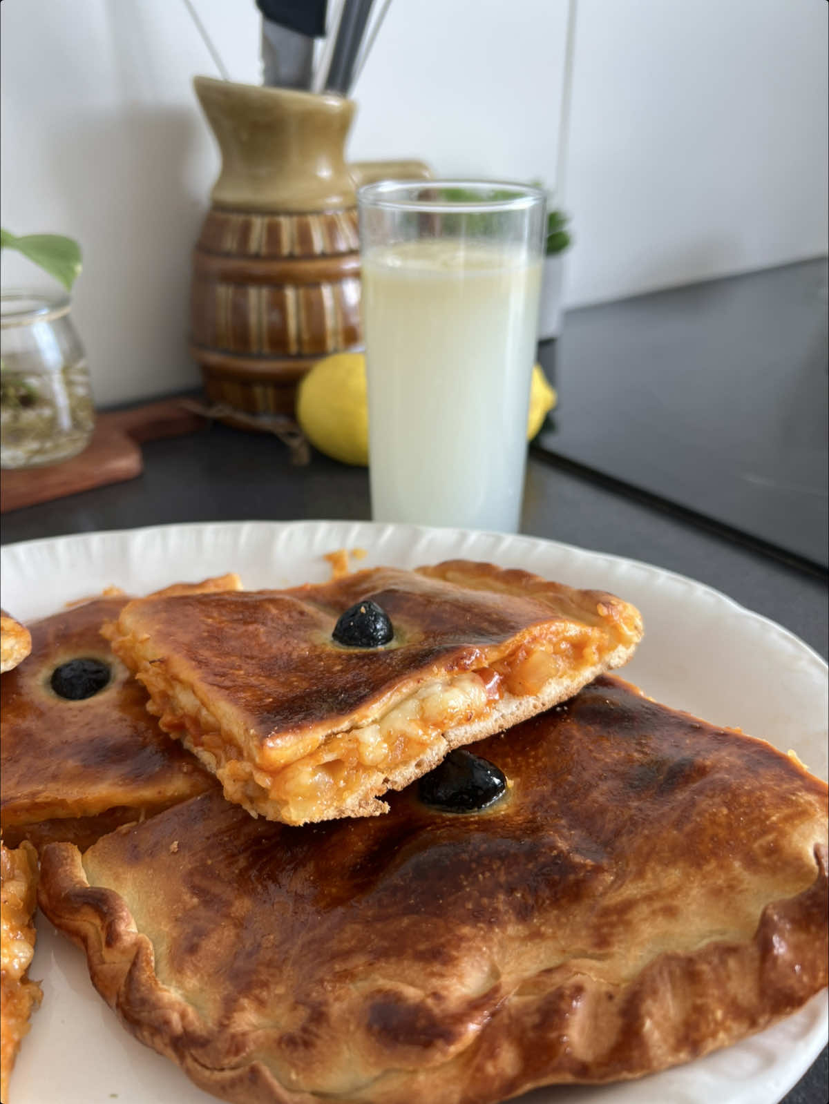 La Coca algérienne 🇩🇿 Je commence par la pâte : je mélange un verre de lait tiède avec une demi-cuillère à soupe de sucre, deux cuillères à soupe de farine et une demi-cuillère à soupe de levure boulangère. Je laisse reposer 10 à 15 minutes pour que la levure s’active. J’ajoute ensuite un quart de verre d’huile, du sel et la farine progressivement jusqu’à obtenir une pâte souple. Je la pétris 5 à 10 minutes, puis je la couvre et je la laisse lever jusqu’à ce qu’elle double de volume. Pour la sauce, je fais revenir 4 gros oignons coupés en dés avec un peu d’huile. J’ajoute 2 tomates en dés, du concentré de tomate, du sel, du paprika et du poivre noir. Je laisse cuire jusqu’à obtenir une sauce bien réduite, puis je la laisse refroidir. Je divise la pâte en deux. J’étale la première partie dans le plat, j’ajoute la sauce et, si je veux, du fromage. Je recouvre avec la deuxième pâte. Je badigeonne de jaune d’œuf, je trace des carrés et j’ajoute quelques olives noires. Je fais cuire à 220 °C, d’abord par le bas environ 20 minutes, puis quelques minutes par le haut pour bien la dorer. نبدأ بالعجينة: نخلط كأس حليب دافئ مع نصف ملعقة كبيرة سكر، ملعقتين كبيرتين فرينة ونصف ملعقة كبيرة خميرة الخبز. نتركها ترتاح 10 إلى 15 دقيقة حتى تتفاعل الخميرة. نضيف بعدها ربع كأس زيت، رشة ملح والفرينة تدريجيًا حتى نتحصل على عجينة طرية. نعجنها من 5 إلى 10 دقائق، ثم نغطيها ونتركها تختمر حتى يتضاعف حجمها. لتحضير الصلصة، نقلي 4 حبات بصل كبيرة مقطعة إلى مكعبات مع قليل من الزيت. نضيف حبتين طماطم مقطعة، الطماطم المركزة، الملح، الفلفل الأحمر الحلو والفلفل الأسود. نتركها تطهى ، ثم نتركها تبرد. نقسم العجينة إلى قسمين. نفتح الجزء الأول ونضعه في الصينية، ثم نضيف الصلصة والجبن حسب الرغبة. نغطيها بالجزء الثاني من العجينة. ندهن الوجه بصفار البيض، ونرسم مربعات بالسكين ونضيف بعض حبات الزيتون الأسود. ندخلها إلى فرن مسخن على 220 درجة، ونشغل الحرارة من الأسفل حوالي 20 دقيقة، ثم نشغل من الأعلى لبضع دقائق حتى تتحمر. #algerienne🇩🇿 #recipes #recette #cocaalgerienne #Foodie 