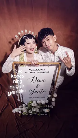 PROMPT: @Sangkara_digitalstudio: Gunakan foto wajah asli pria dan wanita pada lampiran pertama dan kedua sebagai wajah identitas utama masing-masing subjek. Pertahankan identitas wajah 100% akurat, termasuk bentuk wajah, struktur rahang, mata, alis, hidung, bibir, telinga, warna dan tekstur kulit, serta proporsi kepala tanpa perubahan sedikit pun. Buat foto selfie pasangan yang tampak seperti dokumentasi spontan saat persiapan pengantin di ruang tamu rumah beratap plafon, dengan rasio aspek vertikal 9:16. Kamera berada sangat tinggi di atas kepala, mengarah tajam ke bawah menggunakan perspektif ultra-wide 0,5x iPhone, sehingga wajah dan tubuh bagian atas terlihat dari sudut high angle/eye-bird angle. Wanita berada paling dekat dengan kamera dan sedikit condong ke depan, salah satu lengannya menjulur ke arah sudut bawah frame seolah sedang memegang iPhone untuk mengambil selfie. Pria berdiri rapat di belakang atau di samping wanita, sedikit membungkuk mendekati kamera agar kedua wajah masuk dalam frame secara natural. Pertahankan proporsi perspektif khas lensa ultra-wide, dengan lengan yang lebih dekat ke kamera tampak sedikit membesar secara realistis. Wanita mengenakan busana pengantin adat Jawa berwarna putih dengan bahan renda, bordir, dan payet berkilau. Wanita tidak mengenakan hijab dan belum memakai sanggul pengantin final; rambutnya masih diikat menjadi low bun sederhana di bagian belakang kepala, dengan beberapa bagian rambut belum tertata sempurna sehingga terlihat seperti sedang menunggu proses makeup dan pemasangan aksesori selesai. Makeup sudah sebagian diaplikasikan, dengan alis rapi, bulu mata lentik, complexion cukup halus, dan bibir berwarna merah muda natural, tetapi tetap tampak seperti manusia asli. Pria mengenakan busana pengantin yang serasi dengan persiapan adat, terlihat sebagian di samping atau belakang wanita dan mengalung kan lengan nya ke bahu hingga dada wanita. Latar belakang berupa kamar MUA sederhana dengan dinding berwarna putih tulang, kain, tas makeup, serta perlengkapan rias yang tergeletak secara tidak beraturan. Tambahkan beberapa siluet wanita di latar belakang, tetapi wajah mereka tidak terlihat jelas karena posisi membelakangi kamera, terhalang objek, atau sedikit blur. Gunakan kamera depan ultra-wide iPhone 0,5x dengan flash ON sebagai sumber cahaya utama. Flash menghasilkan wajah dan busana yang terang, sedikit highlight berlebih pada kulit serta renda putih, bayangan keras di dinding, dan latar belakang harus lebih gelap karena efek yang dihasilkan dari flash. Pertahankan karakter foto smartphone spontan: tidak ada pencahayaan yang mecolok di latar belakang, warna sedikit dingin dramatis, kontras sedang, detail tidak terlalu tajam, noise digital halus, sedikit motion blur, dan ketidaksempurnaan exposure yang wajar. Hasil akhir harus terlihat seperti foto asli yang diambil terburu-buru di kamar persiapan pengantin, bukan foto studio profesional atau hasil retouch berlebihan. Negative Prompt: identitas wajah berubah, wajah generik AI, perubahan bentuk mata, hidung, bibir, rahang, atau proporsi kepala, kulit plastik, beauty filter berlebihan, wajah terlalu mulus, makeup pengantin yang sudah sempurna, hijab, sanggul pengantin yang sudah terpasang sempurna, rambut terlalu rapi, aksesori pengantin hilang, rangkaian melati tidak akurat, busana berubah warna, renda dan payet tidak realistis, pose selfie salah, lengan tidak menjulur ke arah kamera, tangan terpotong secara tidak wajar, jari tambahan, jari menyatu, anatomi tangan rusak, perspektif ultra-wide tidak akurat, kamera sejajar mata, pencahayaan studio, cahaya lembut berlebihan, latar belakang kamar hotel mewah, wajah orang di belakang terlalu jelas, duplikasi orang, HDR berlebihan, oversharpening, resolusi terlalu sempurna, noise berlebihan, blur berlebihan, efek CGI, tekstur kulit buatan, artefak digital, dan tampilan gambar AI. #prompt #AI #gemini #argon #chatgpt